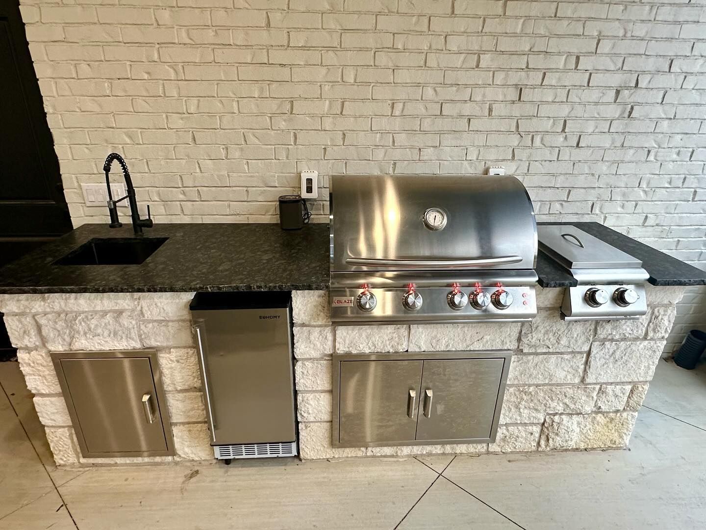 Outdoor kitchen with a stainless steel grill, sink, and stone facade.