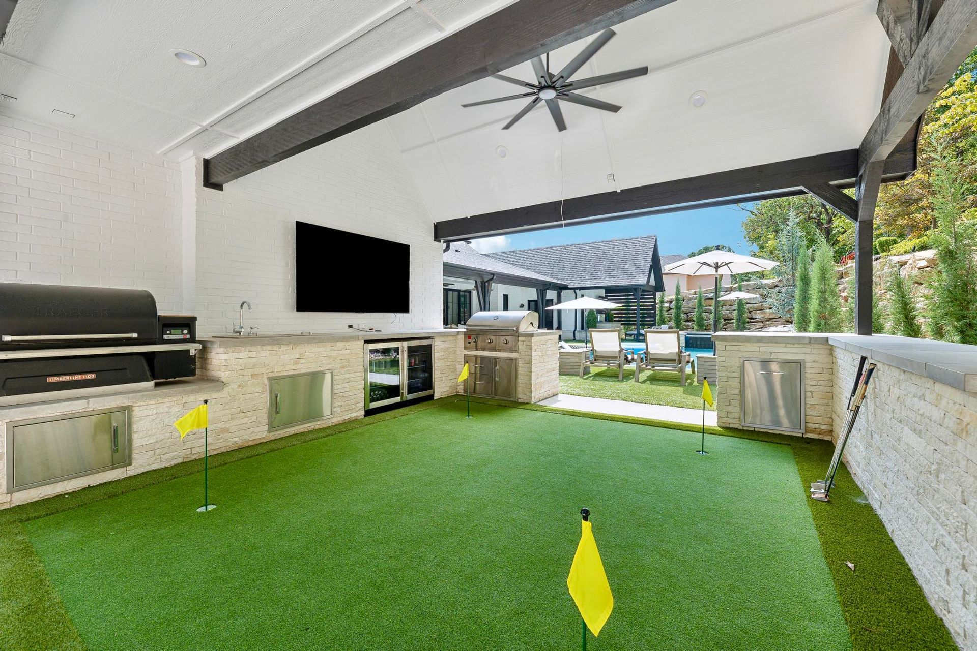 Outdoor area with putting green, grill, TV, and seating; sunny day.