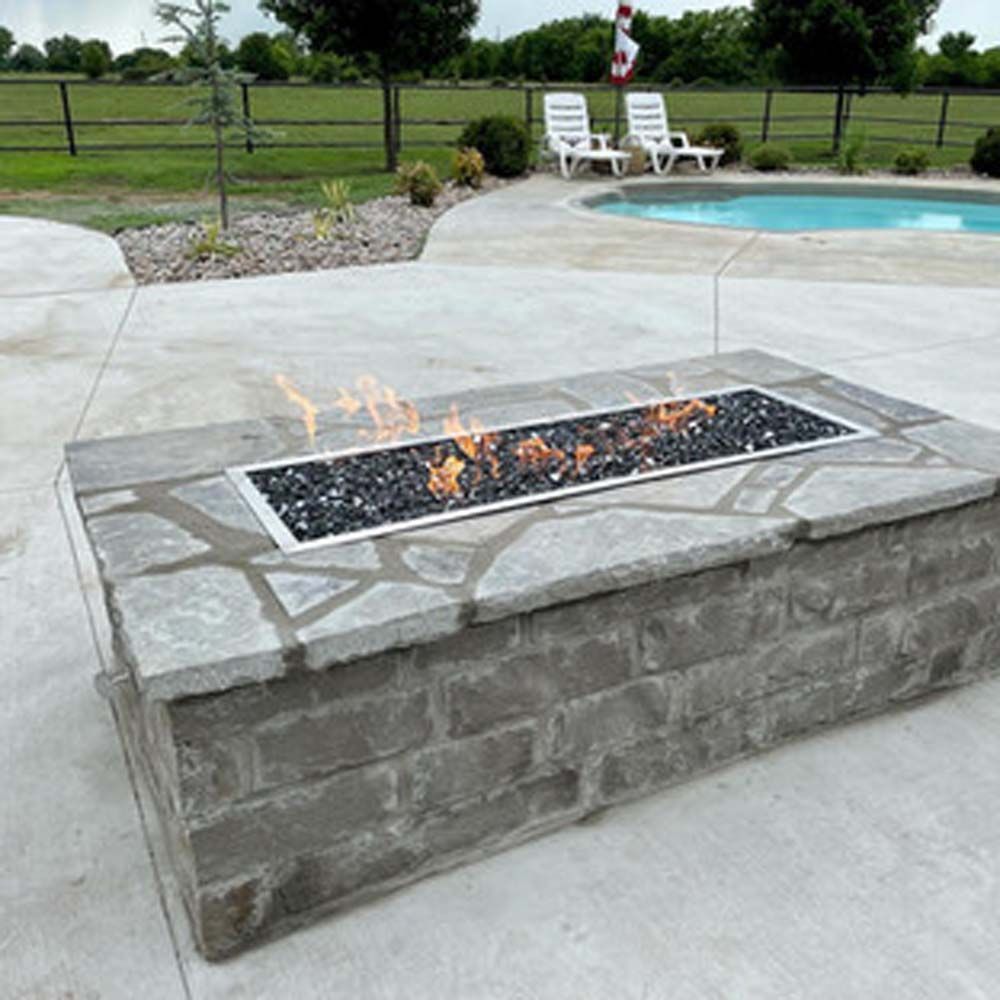 Stone fire pit with flames, near a pool and lounge chairs. Outdoors.
