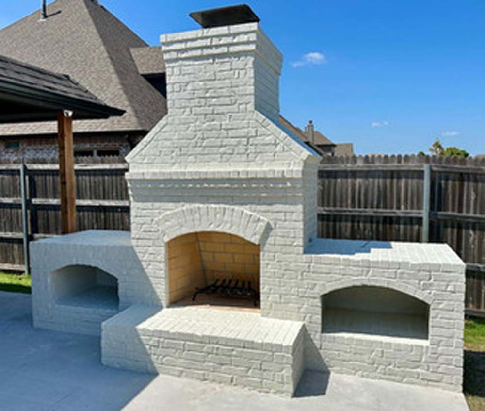 White brick outdoor fireplace with oven and storage areas on a patio.