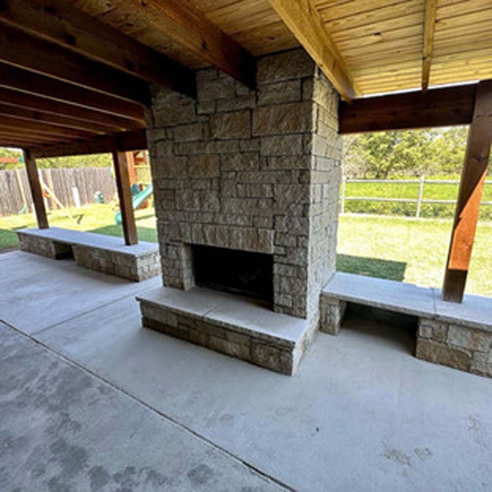 Stone fireplace with benches on a covered patio, backyard in view.