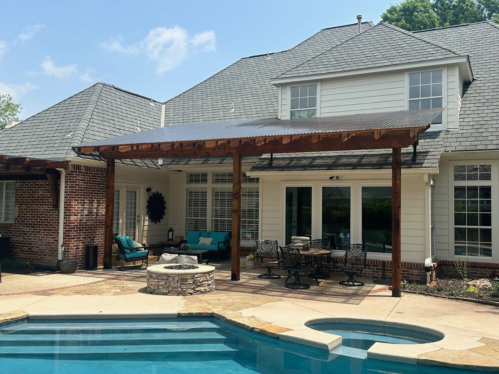 Backyard patio with pergola, pool, and house. Wooden structure, outdoor furniture, blue water.