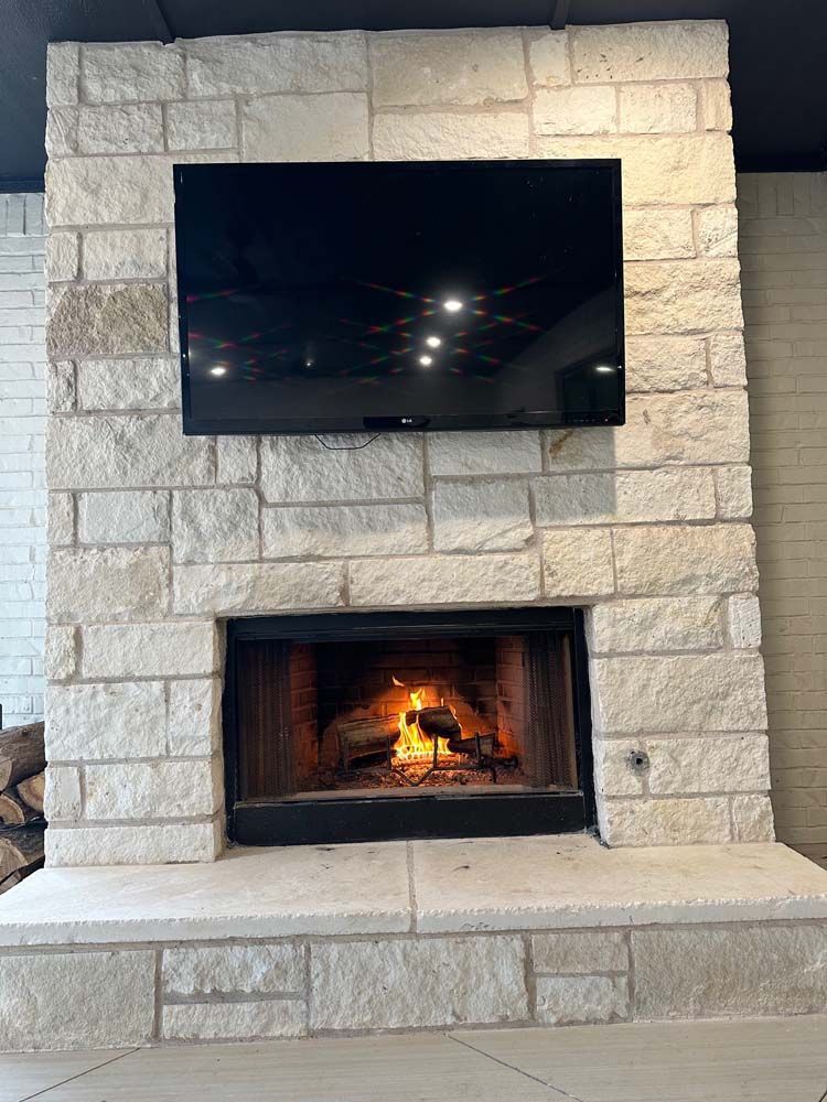 Fireplace with burning fire, stone surround, and mounted TV.