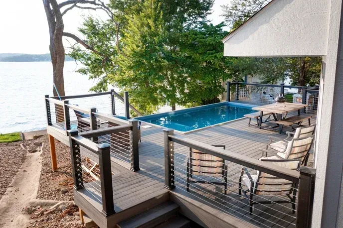 A rectangular pool with steps sits in a concrete patio, surrounded by a forest.