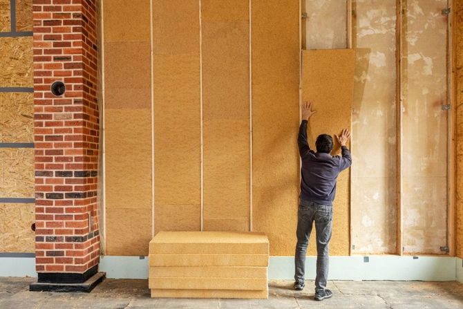Worker installing large tan wall panels in a building interior