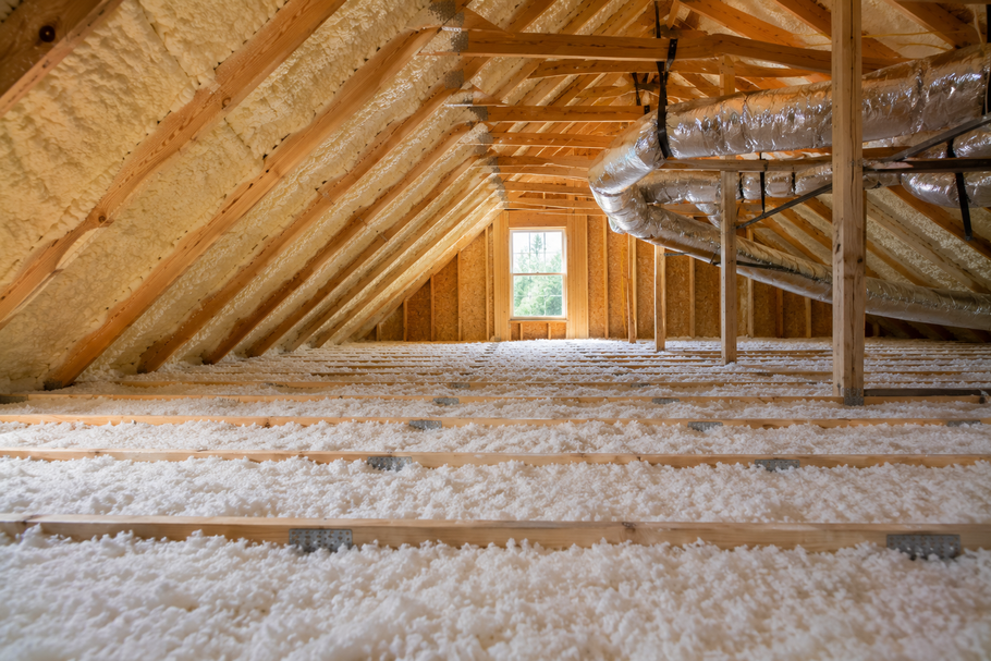 Worker in orange suit spraying foam insulation into an attic rafters area