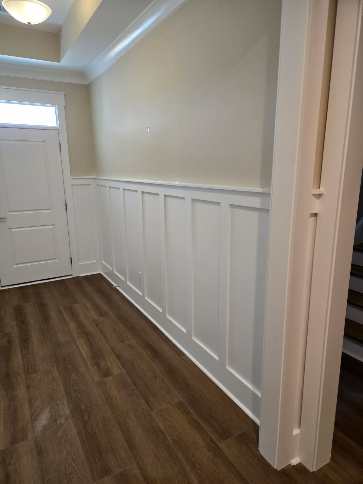 Entryway with white paneling on wall and wood-look flooring. Light-colored walls and door.