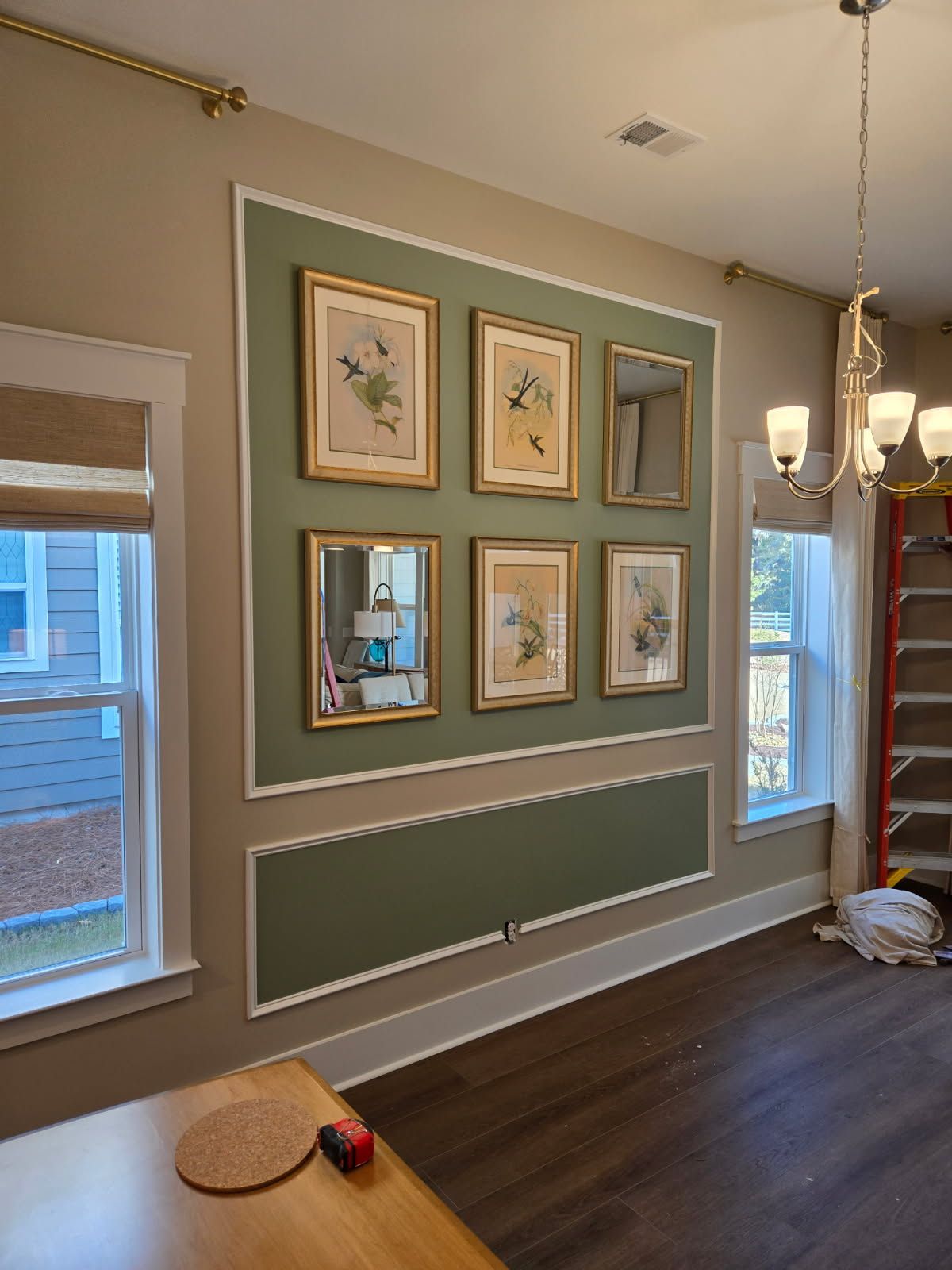Dining room wall with framed art and mirrors, painted olive green with white trim.