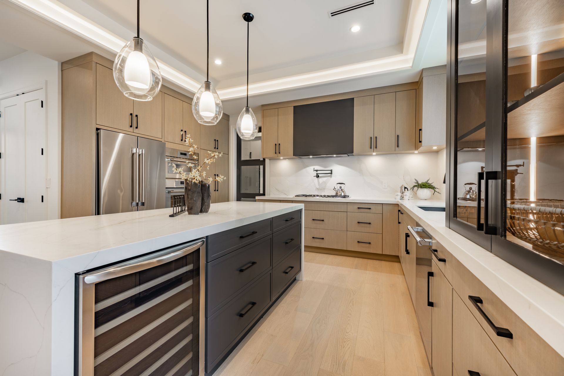 Modern kitchen with a gray island, light wood cabinets, stainless steel appliances, and pendant lights.
