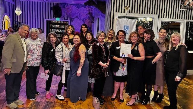 A group stands in a room with striped walls, holding a certificate while posing for a photo.