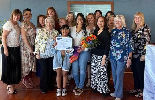 Group of people posing indoors with flowers and a certificate, smiling at a celebration event.