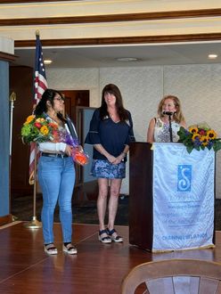 Three people stand on a wooden stage with a podium and American flag during a presentation or award ceremony.
