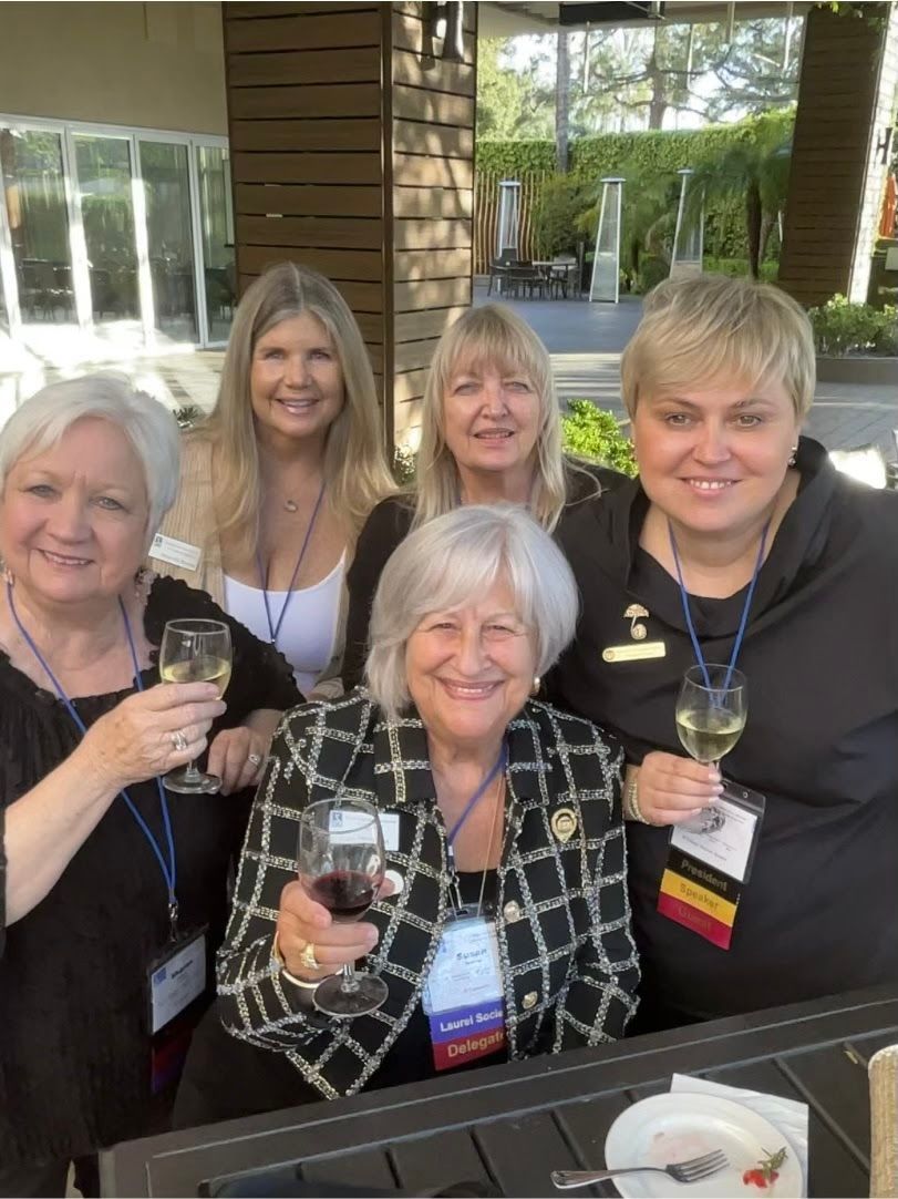 Five people smile and hold glasses of wine while standing together on a patio, wearing name tags on lanyards.