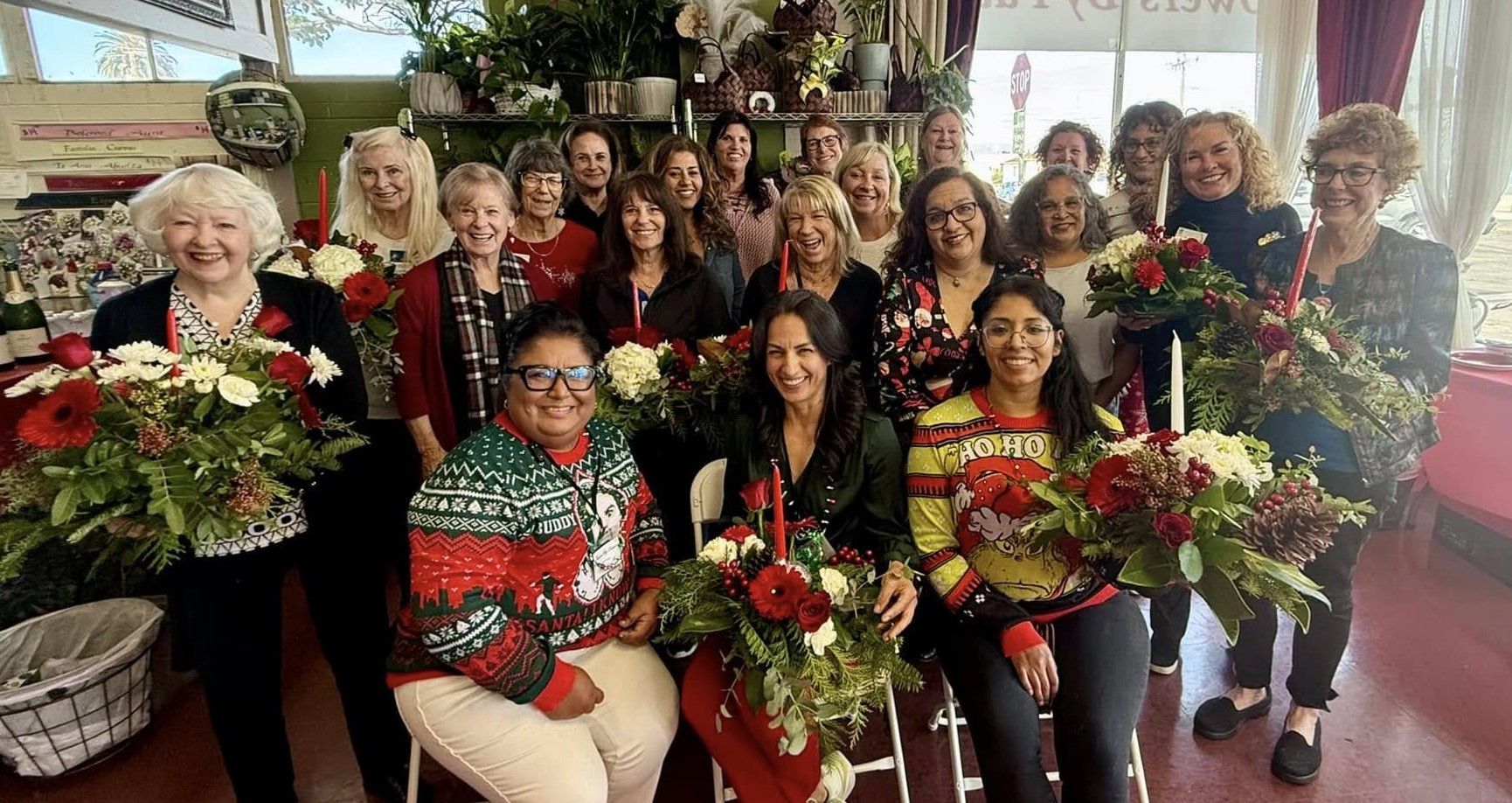 A group of people standing together in a floral shop, smiling and holding bouquets of flowers.