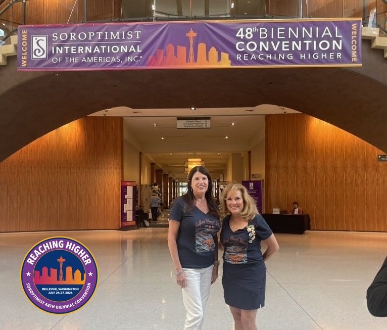 Two people standing before a Soroptimist International of the Americas 48th Biennial Convention banner in a lobby.