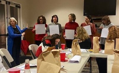People standing in a meeting room, holding papers in front of a seated audience.