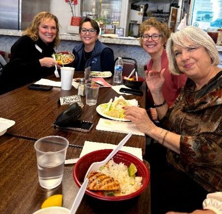Four people sitting around a wooden table in a restaurant, smiling while eating meals together.