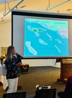 A presenter stands before a large projection screen displaying a map of the California Channel Islands.