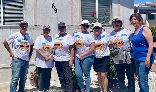 Seven people stand in a line smiling in front of a house numbered 69, most wearing white