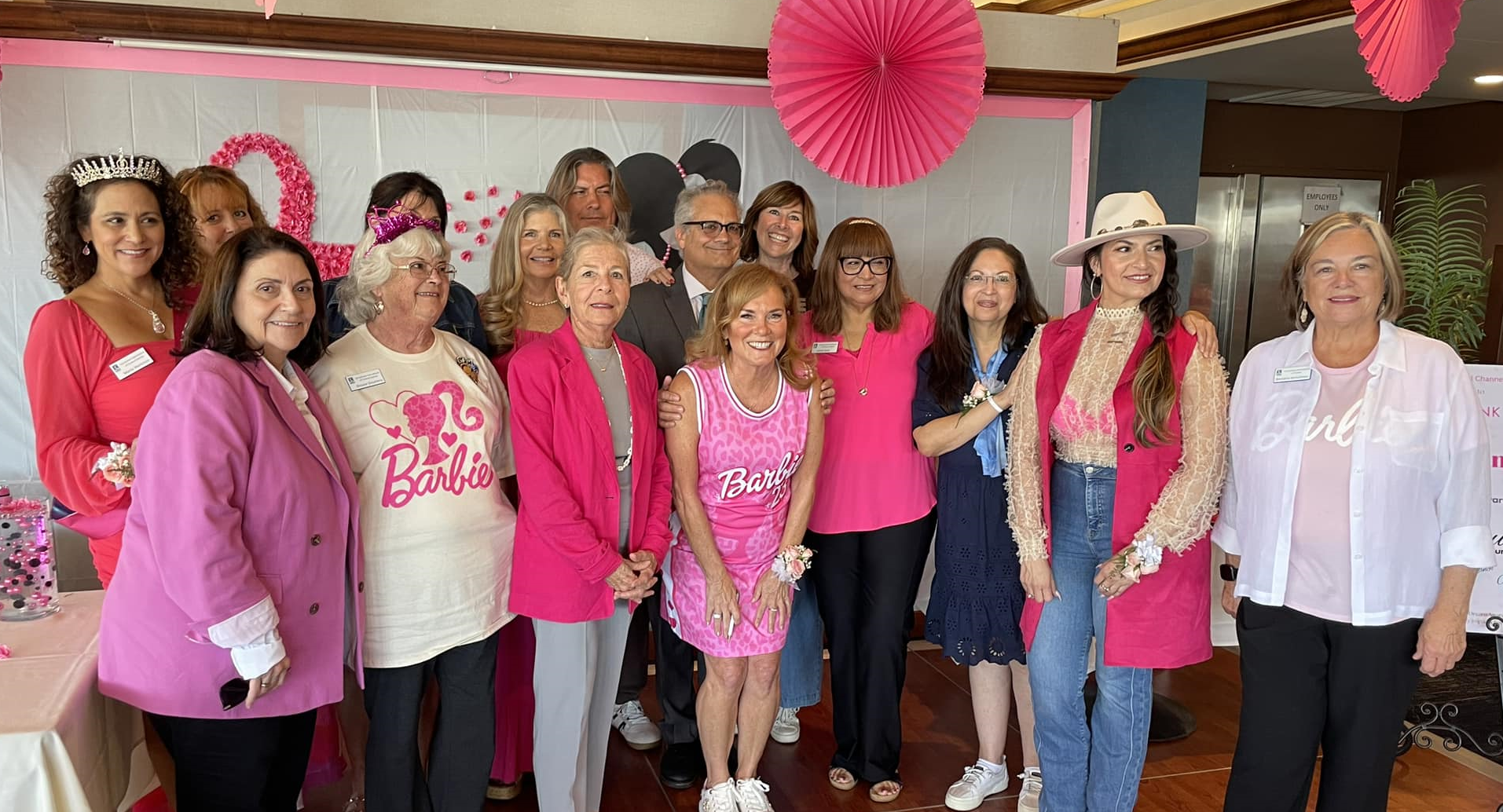 A group of people wearing pink and Barbie-themed outfits standing together at a festive indoor event.