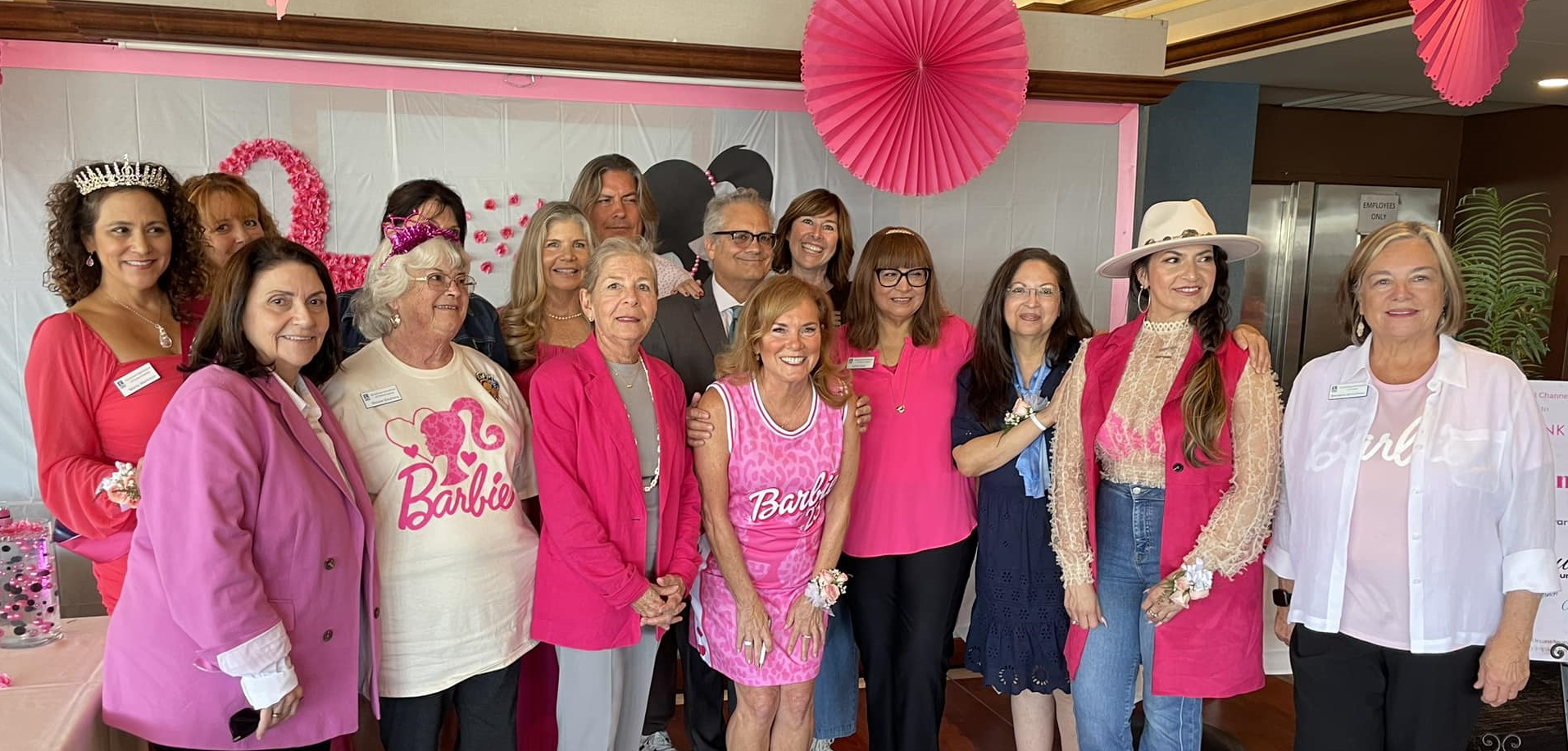 A group of people wearing pink and casual attire standing in front of pink decorations for an event.