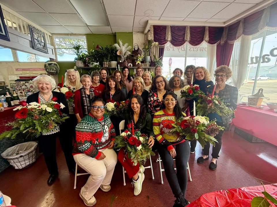 A group poses with floral arrangements inside a flower shop during a holiday event.