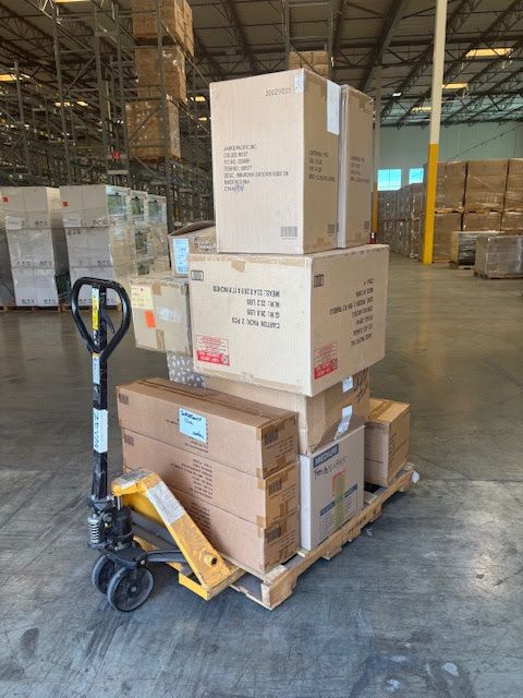 A pallet jack carrying a stack of cardboard boxes in a warehouse setting.