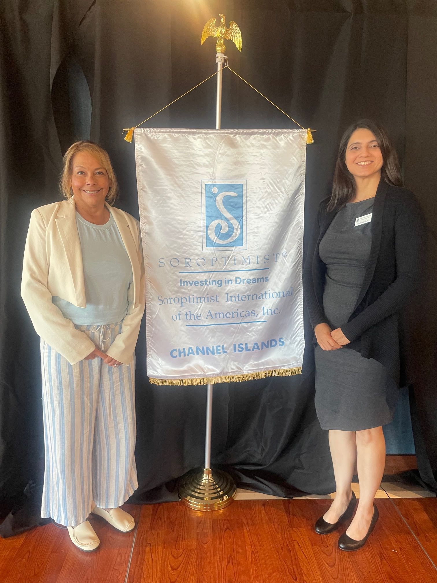 Two people stand smiling on either side of a white ceremonial banner