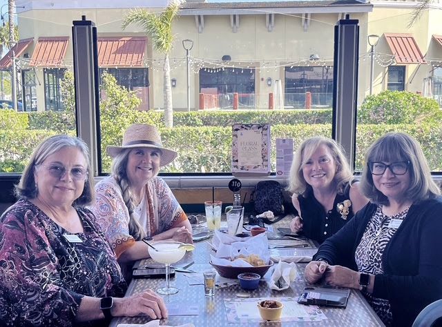 Four people sit around a table at an outdoor restaurant, smiling and enjoying a meal together.