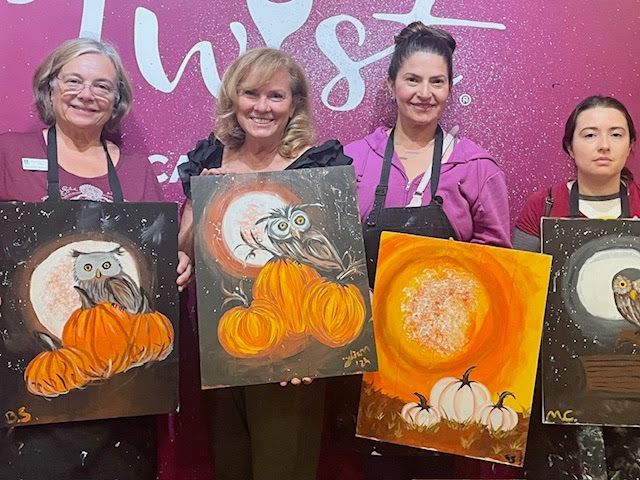 Four people hold owl-themed Halloween paintings while standing in front of a Painting with a Twist sign.