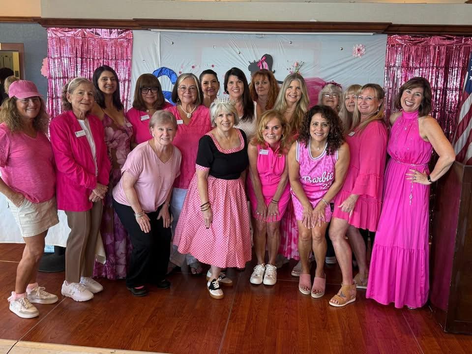 A group of people wearing various shades of pink standing in a room with pink decorations and a flag.