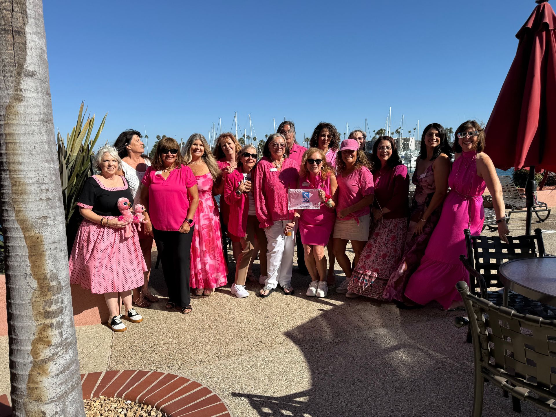 A group of people wearing pink standing outdoors on a sunny day for a photo, with some holding a small sign.
