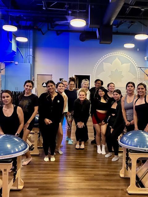 A group of people standing in a studio with exercise equipment, smiling together after a fitness class.