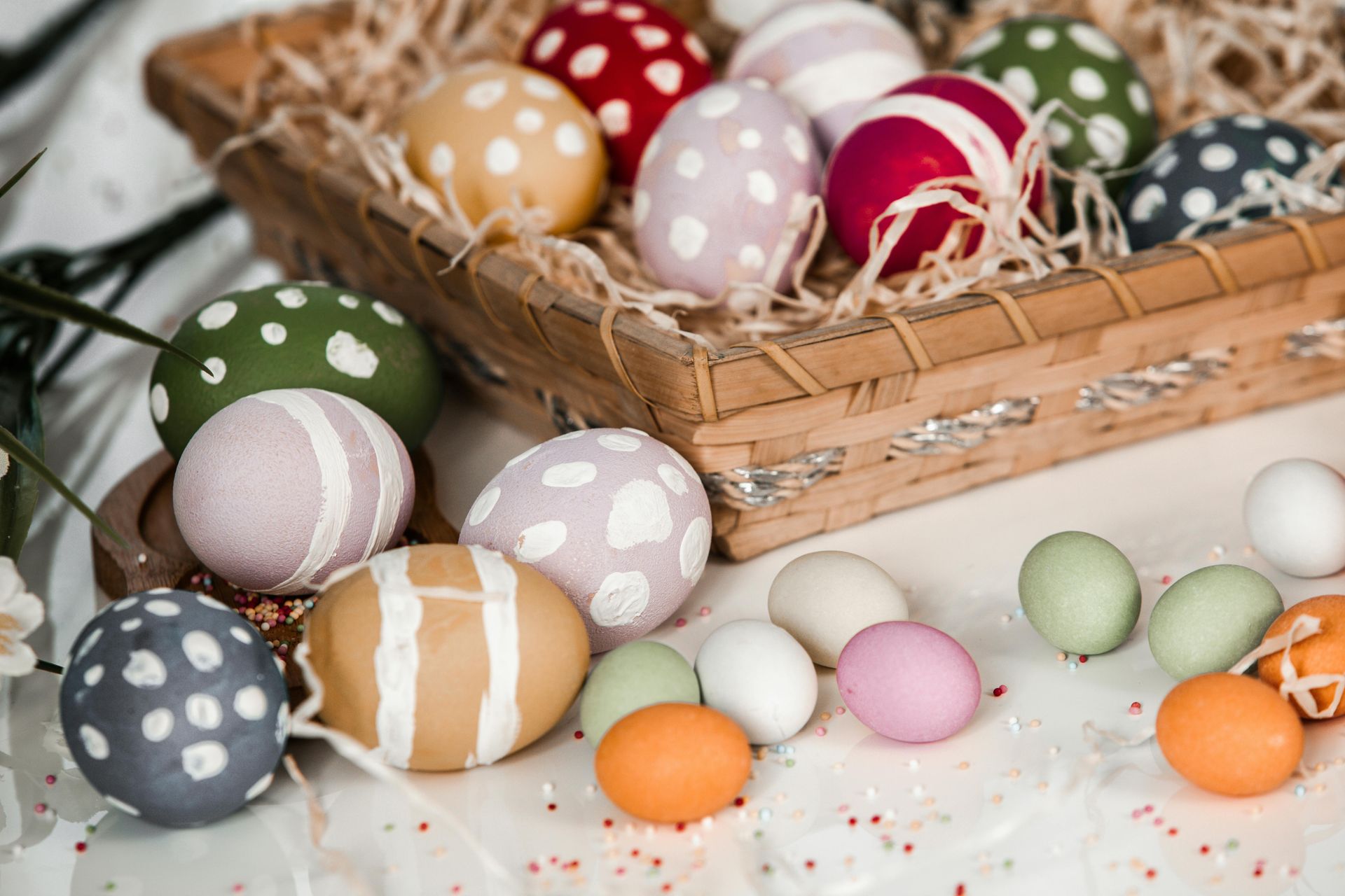 A basket filled with various patterned and colorful Easter eggs, surrounded by smaller, solid-colored eggs on a table.