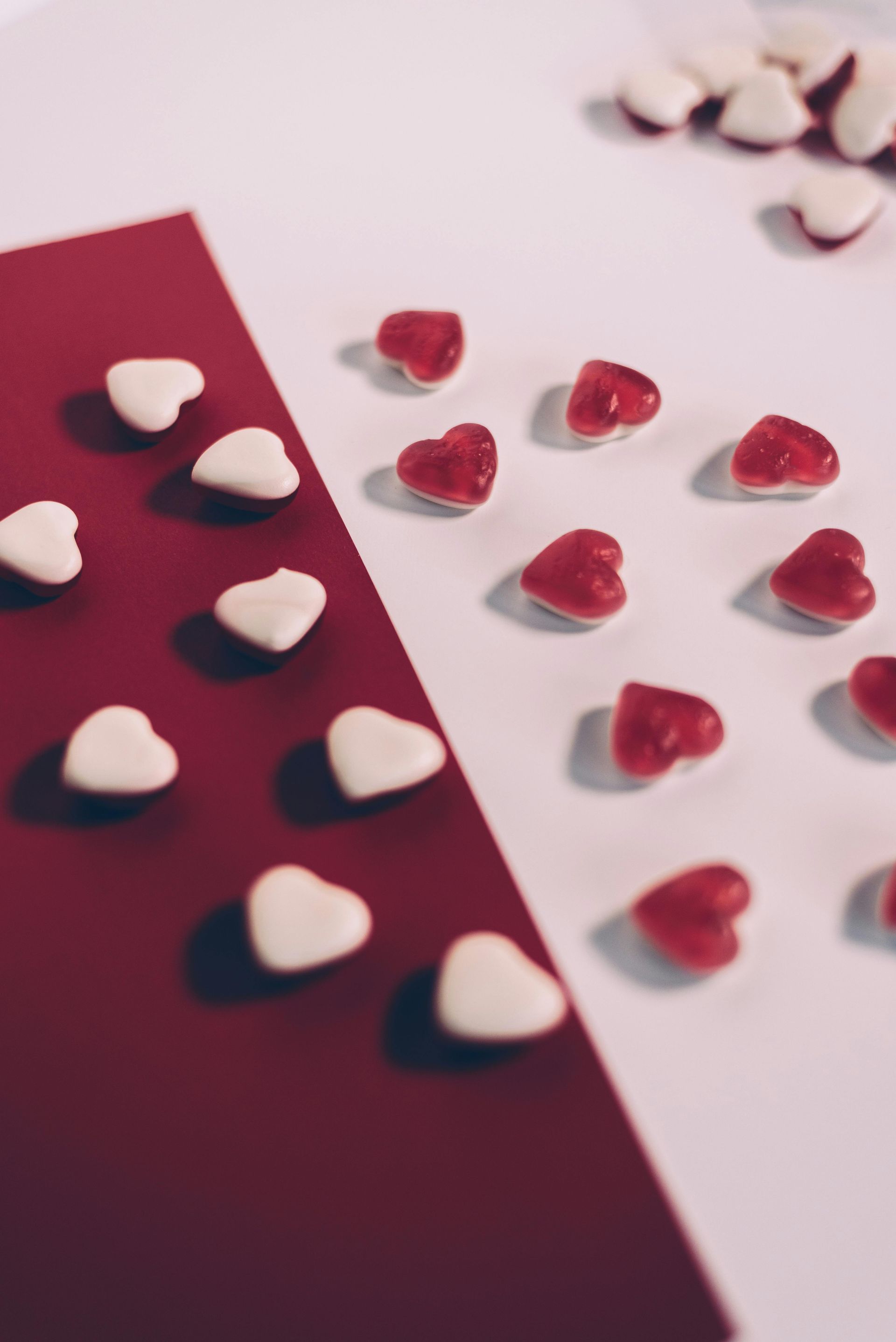 Small white and red heart-shaped candies arranged on a split-tone red and white background.