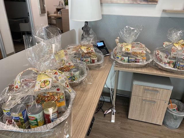 Four gift baskets filled with canned goods and food items, wrapped in clear plastic, sitting on an office desk.