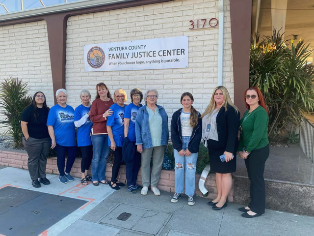 A group of ten people stand smiling in front of the Ventura County Family Justice Center building sign.