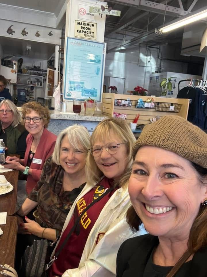 A group of four smiling people sitting at a restaurant table, with one person in the foreground taking a selfie.