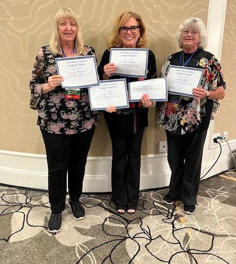 Three people stand side-by-side in a room, smiling and holding award certificates.