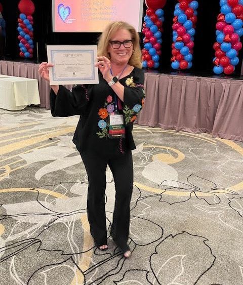 A smiling person holds a certificate in a room decorated with red and blue balloon columns.