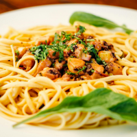 Spaghetti topped with meat sauce and herbs, garnished with basil leaves on a white plate