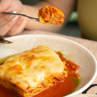 Fork lifting cheesy lasagna from a bowl of red tomato sauce