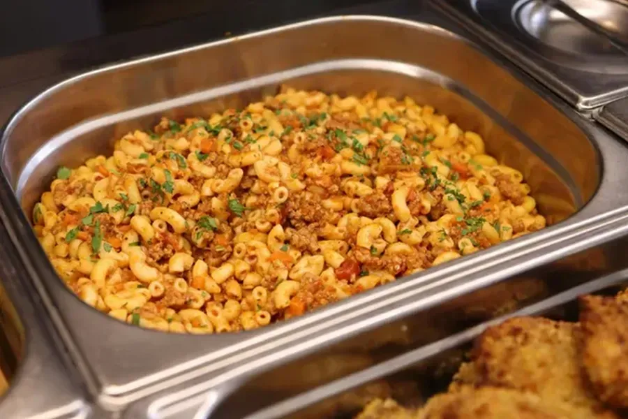 Tray of macaroni salad with peas and diced vegetables at a buffet counter
