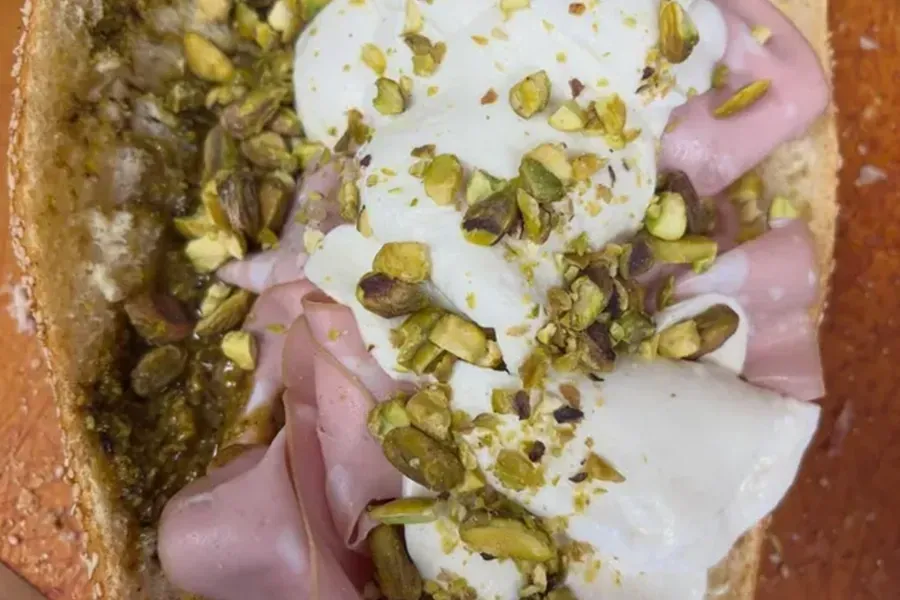 A close-up of a pistachio-topped dessert with pink and white cream in a crusted dish