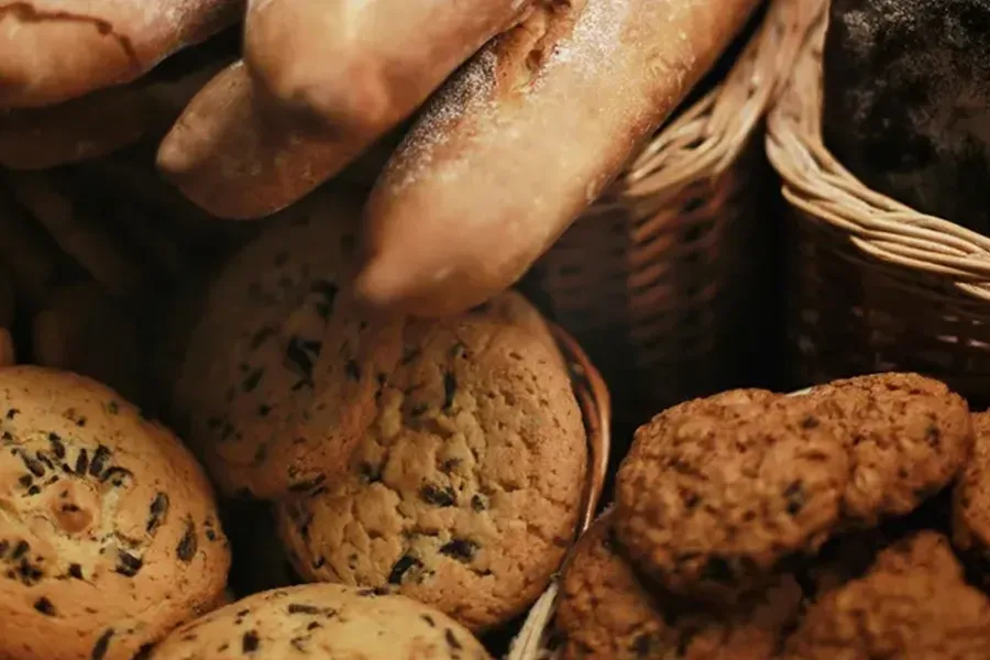 Assorted fresh bread and cookies in a wicker basket, warm-toned close-up.