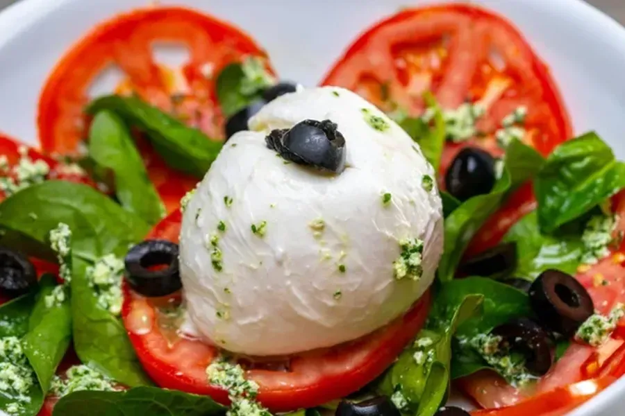 Greek salad with tomato slices, cucumber, olives, and a white mozzarella ball on a plate