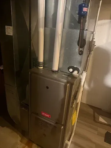 A Bryant furnace in a utility room with white PVC pipes and gray metal ductwork.