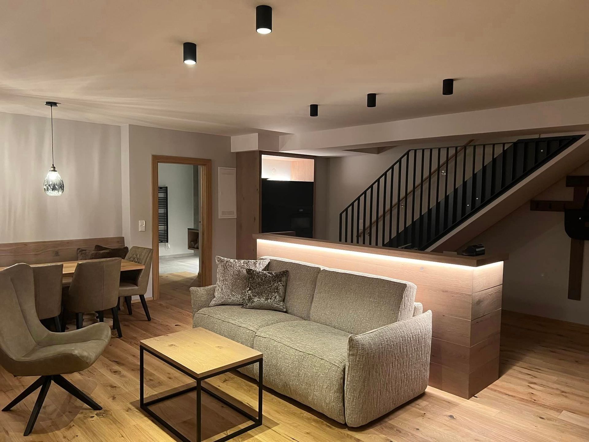 Ein Wohnzimmer mit Couch, Sessel, Tisch und Treppe.