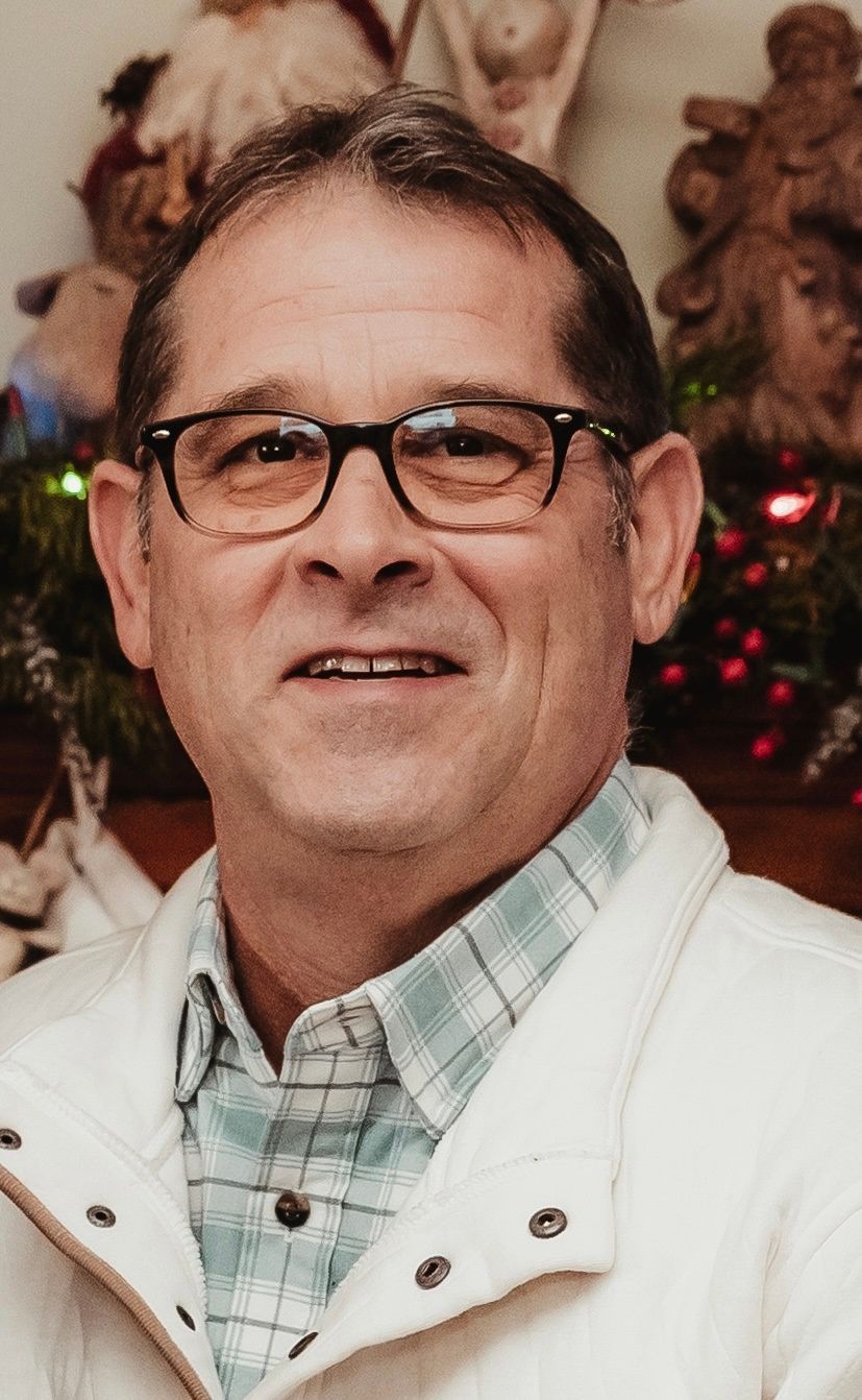 Man in glasses smiling, wearing a blue shirt, tie, and dark suit jacket.