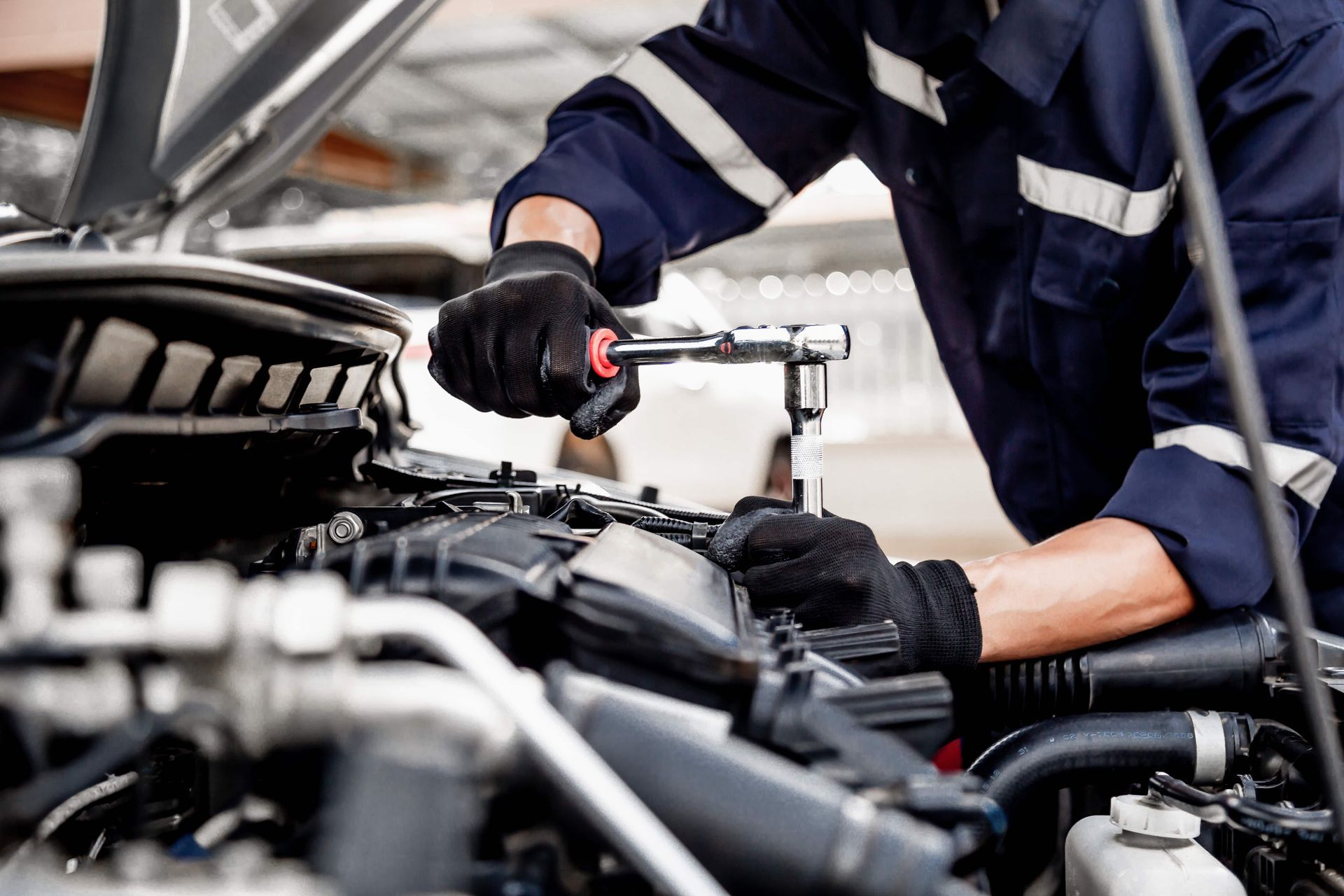 Mechanic working on a car engine with a wrench. Wearing gloves and blue jumpsuit.